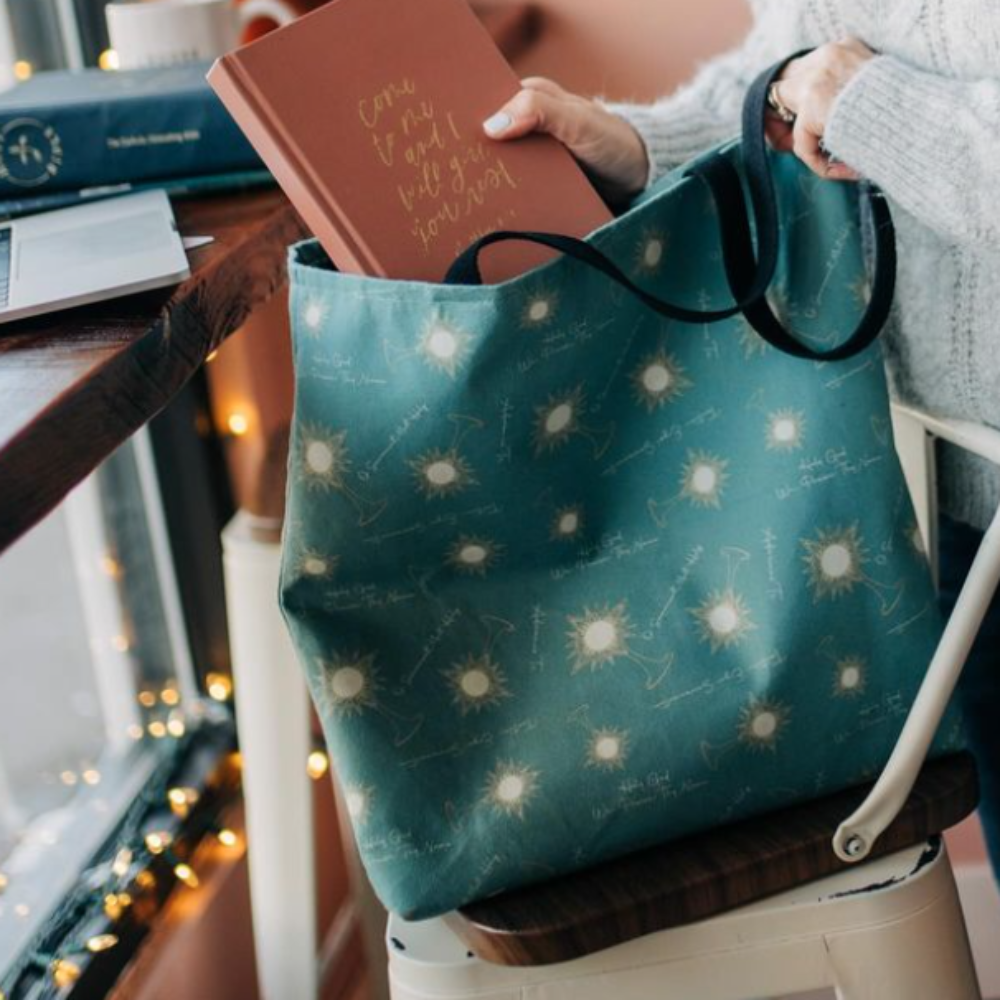 A woman putting a planner into the Adoremus Catholic tote featuring a monstrance pattern