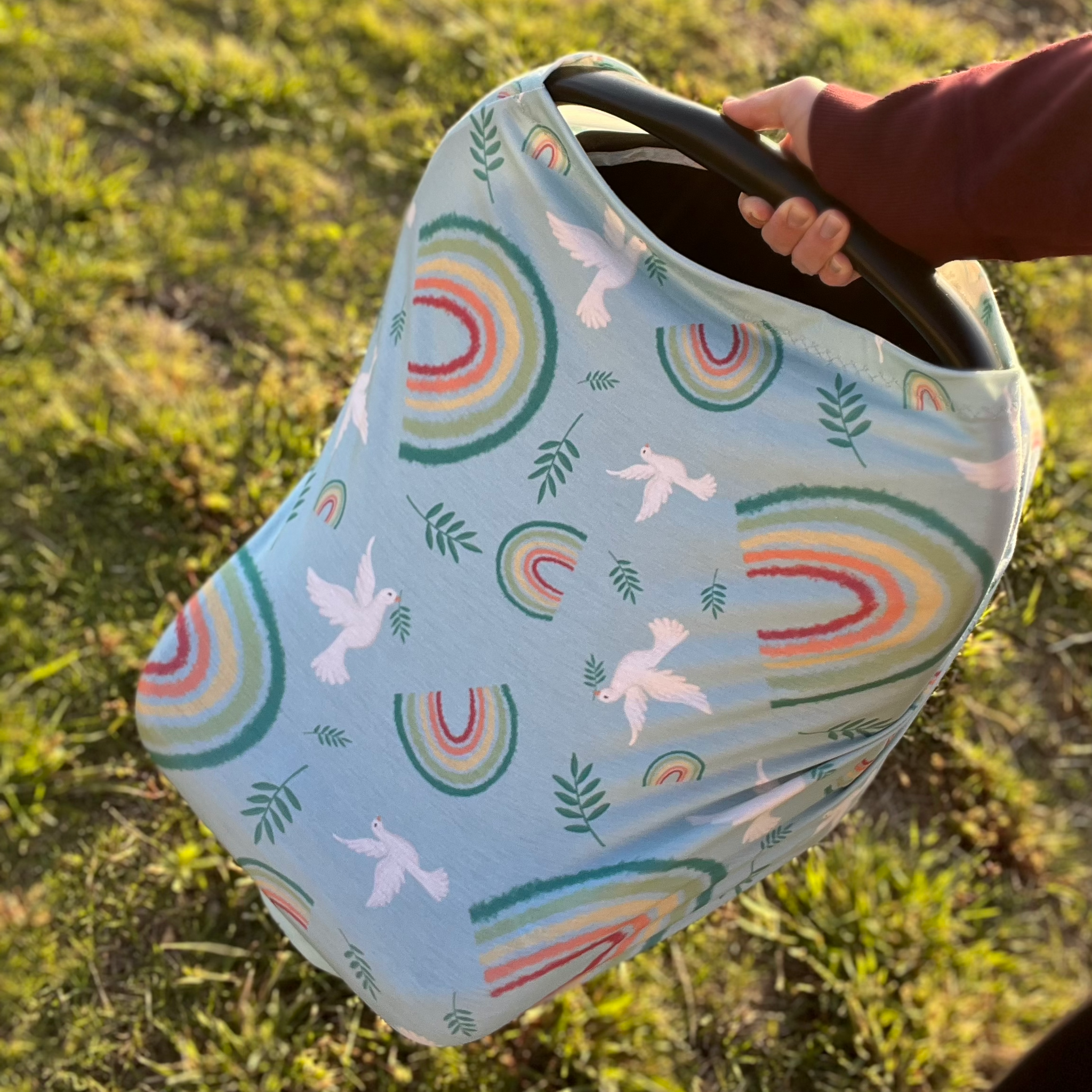 A woman holding a car seat wrapped in a Catholic car seat/nursing cover
