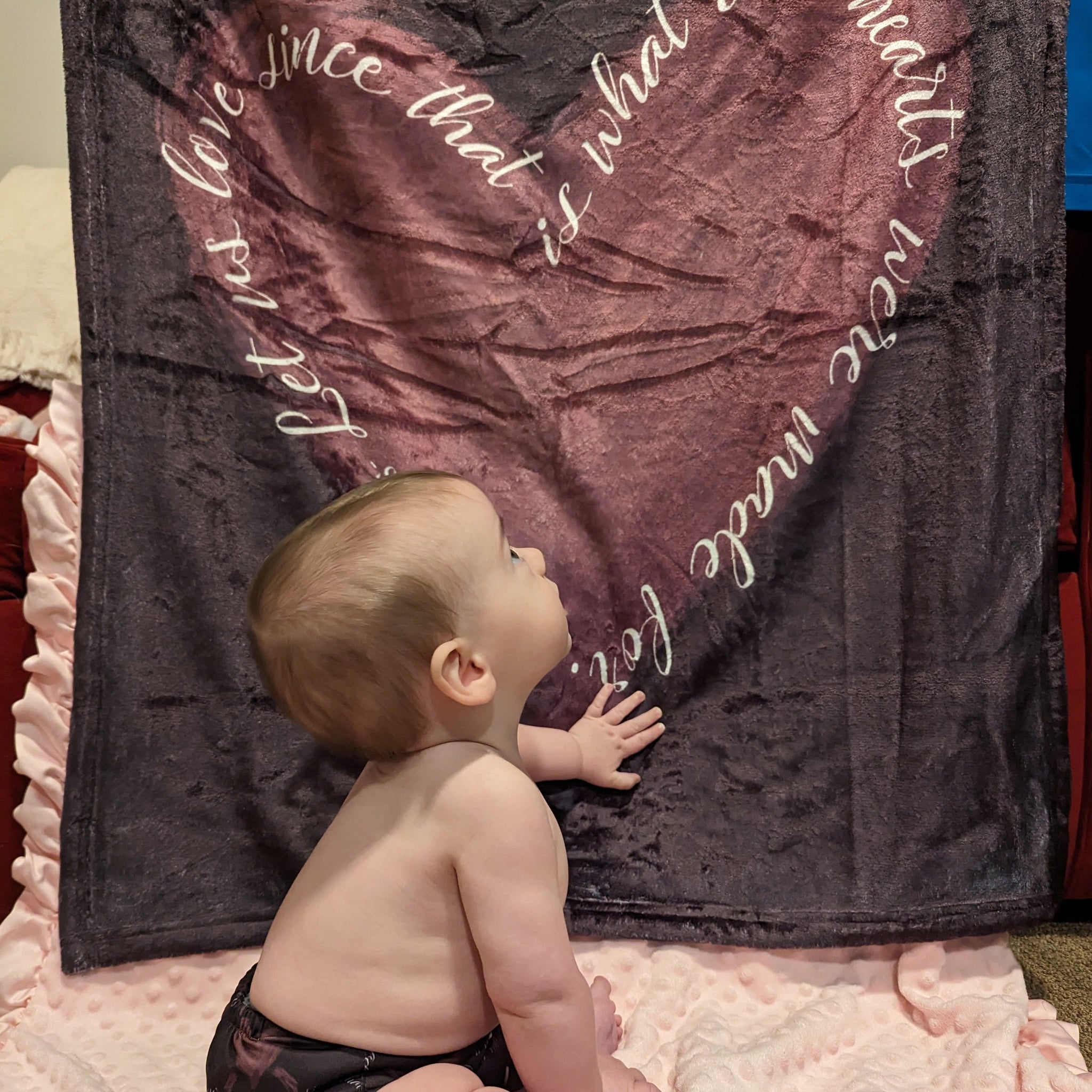 A baby near a blanket that features St. Therese's Let Us Love quote with a heart