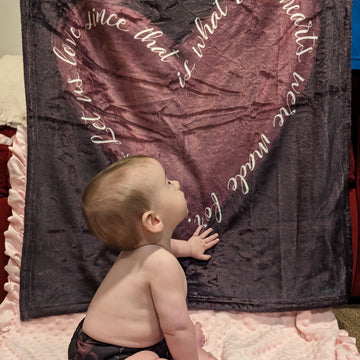 A baby near a blanket that features St. Therese's Let Us Love quote with a heart